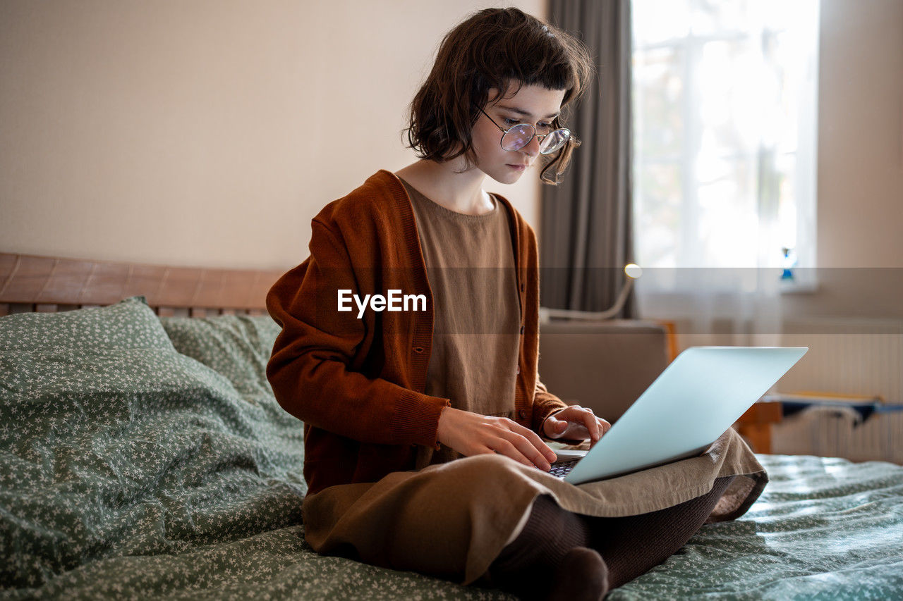 Concentrated pensive teen girl working as freelancer, studying online at home using laptop computer