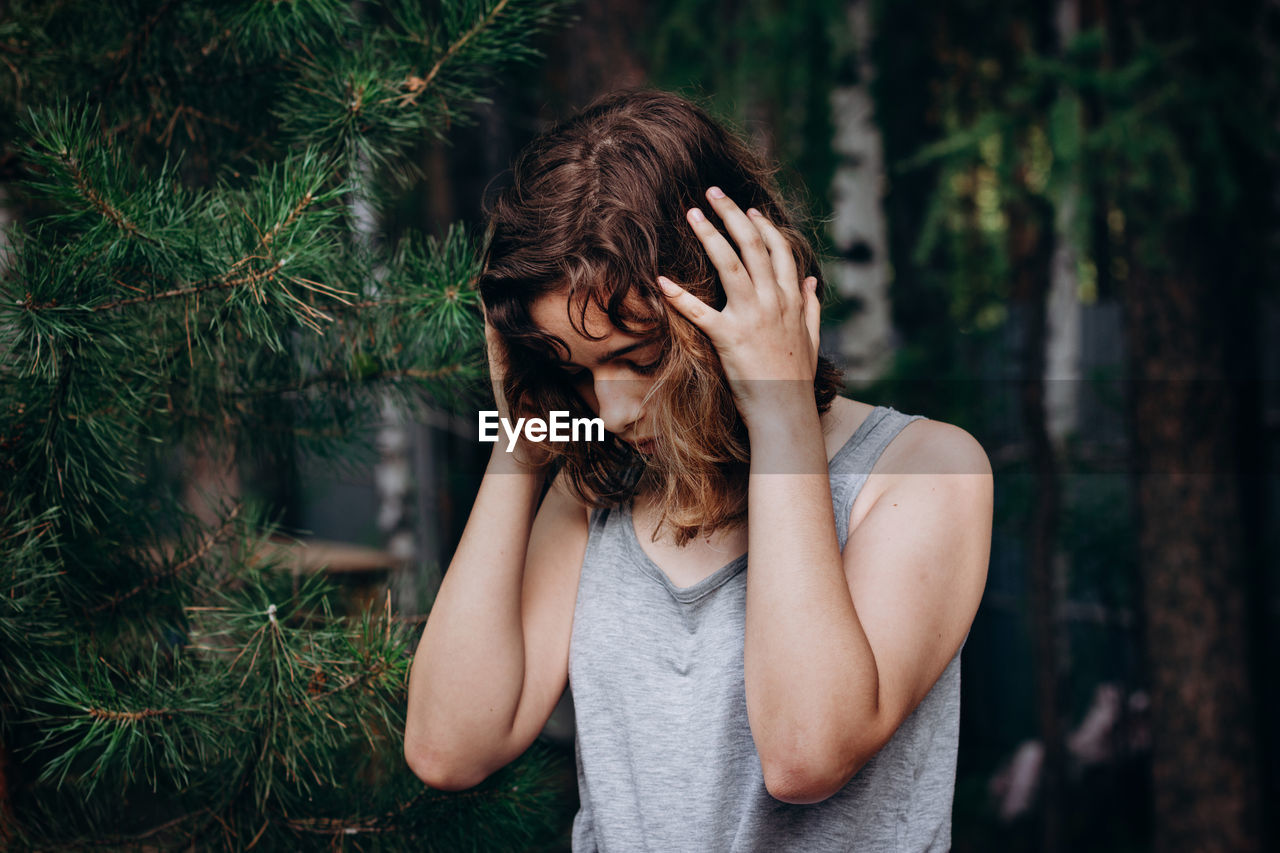 Young woman looking away while standing against trees