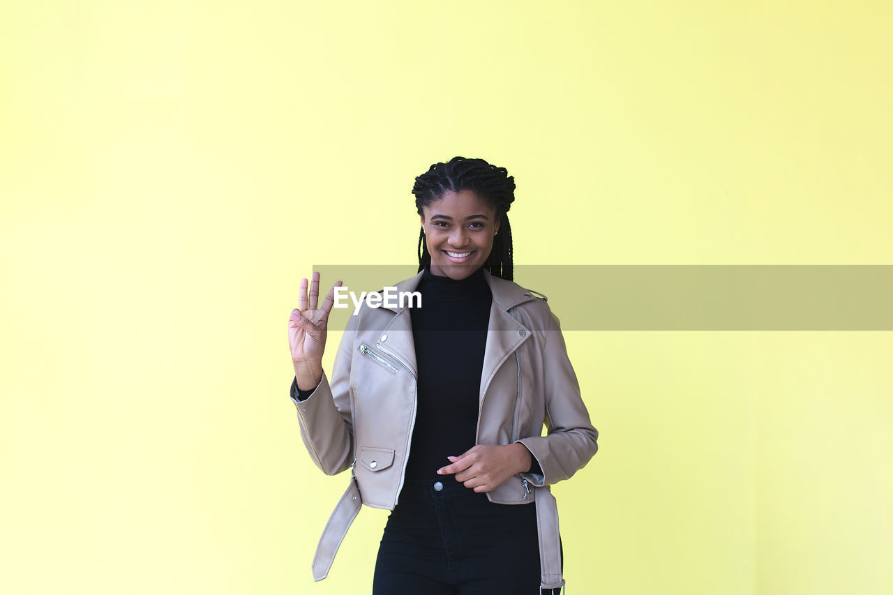 PORTRAIT OF SMILING YOUNG WOMAN STANDING AGAINST GRAY BACKGROUND