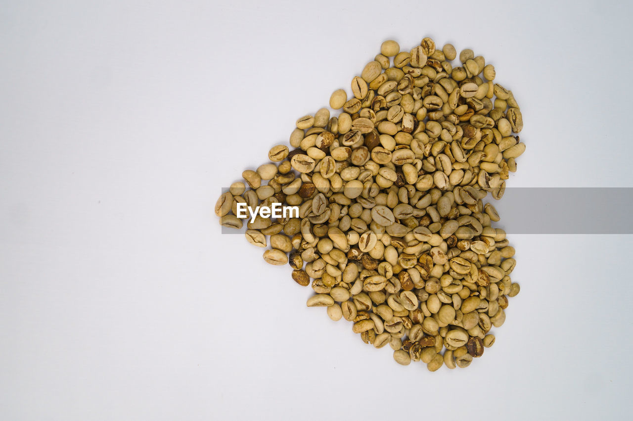 High angle view of raw coffee in heart shqpee against white background