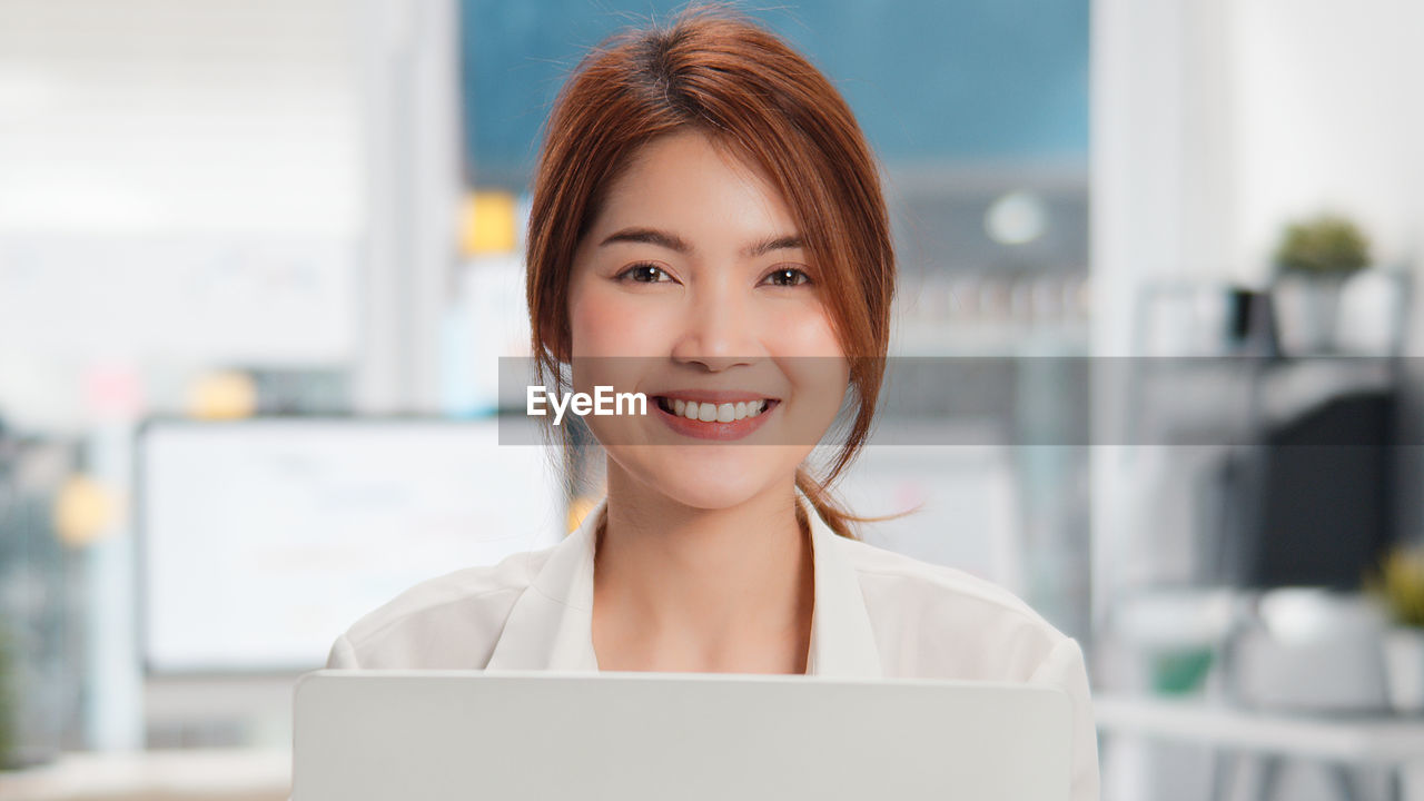 PORTRAIT OF A SMILING YOUNG WOMAN USING LAPTOP