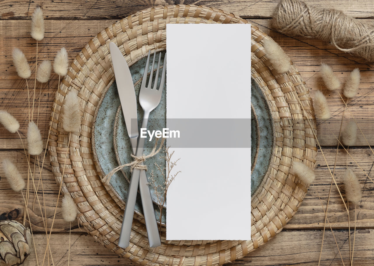 Blank menu card on plate on wooden table with bohemian decorations and dried plants