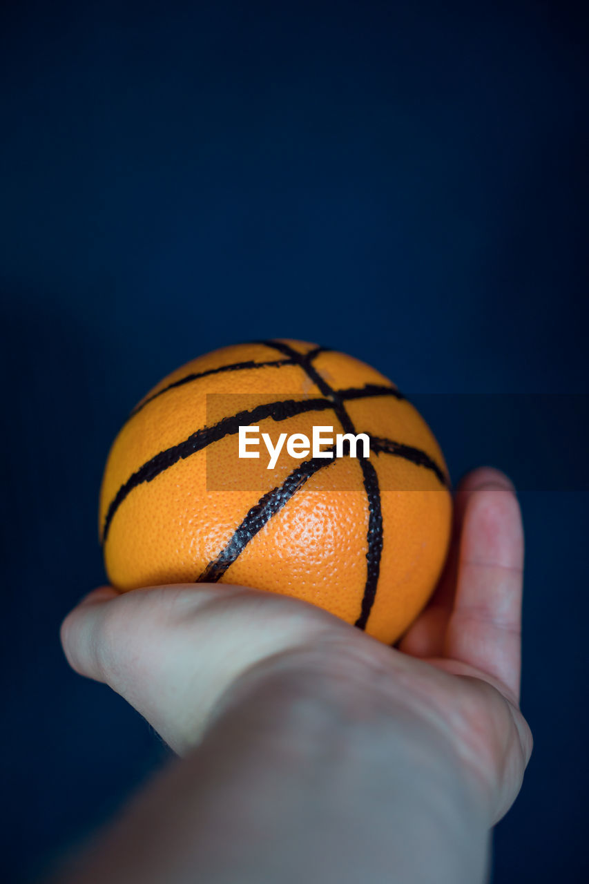 CLOSE-UP OF PERSON HAND HOLDING BALL AGAINST CLEAR BLUE BACKGROUND