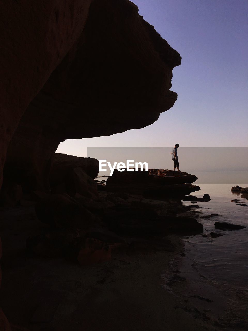 Side view of man standing on cliff by sea during sunset