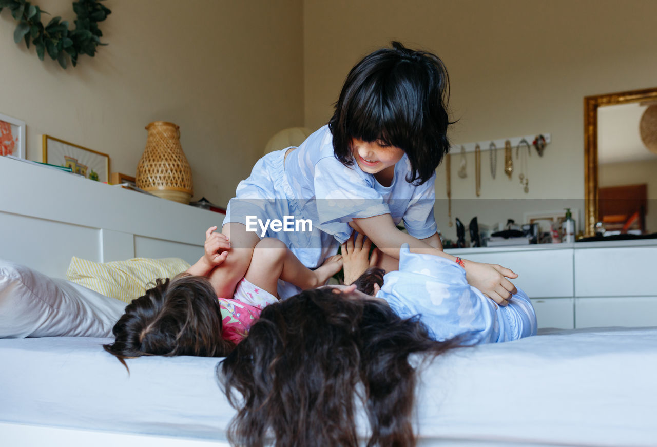 Two children lying on the bed and other child jumping over