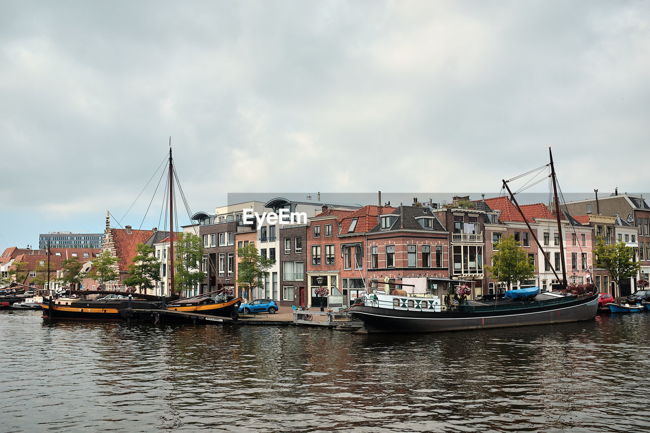 SAILBOATS MOORED IN RIVER AGAINST BUILDINGS IN CITY