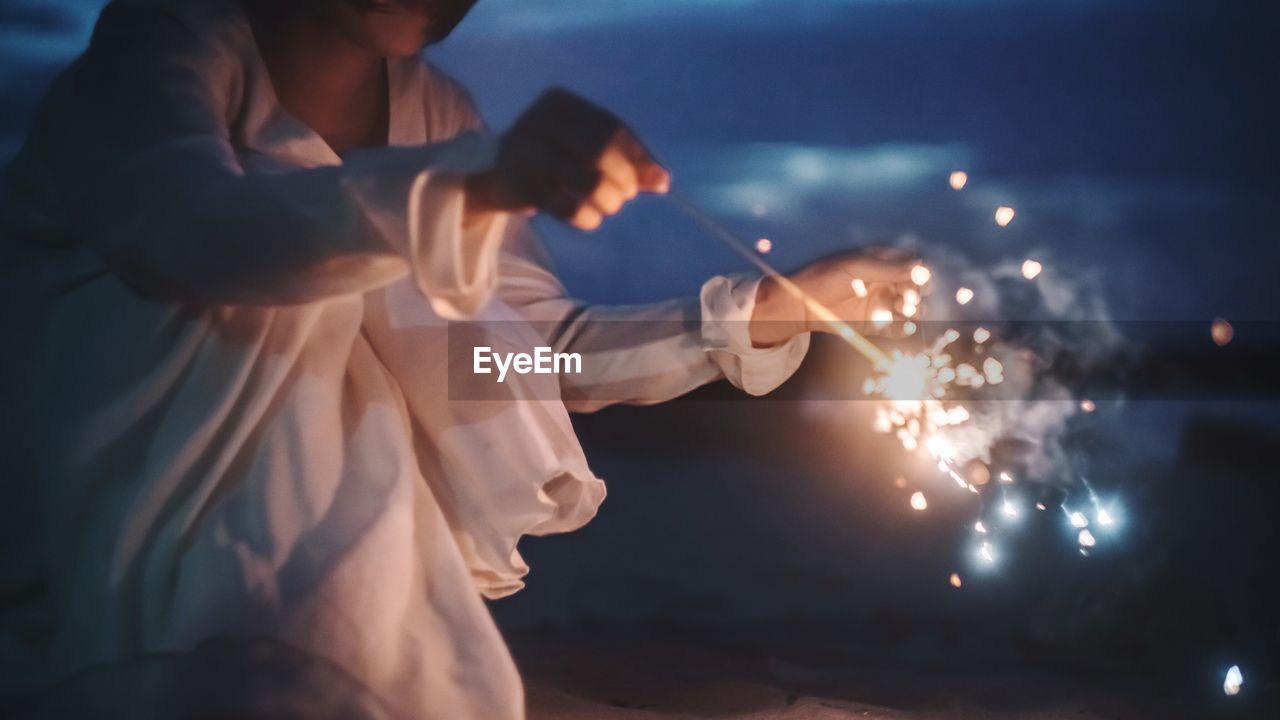 Midsection of woman holding sparkler at night