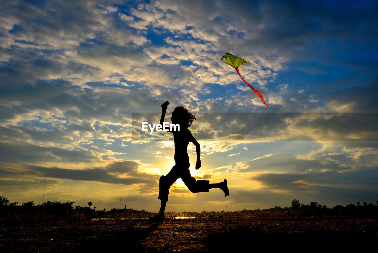 Silhouette girl holding kite while running on land against sky during sunset