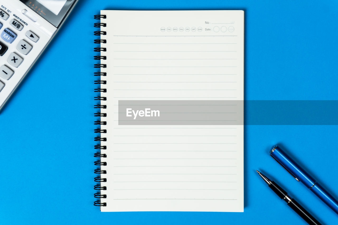 Open notebook with calculator and pen from top view on blue background.