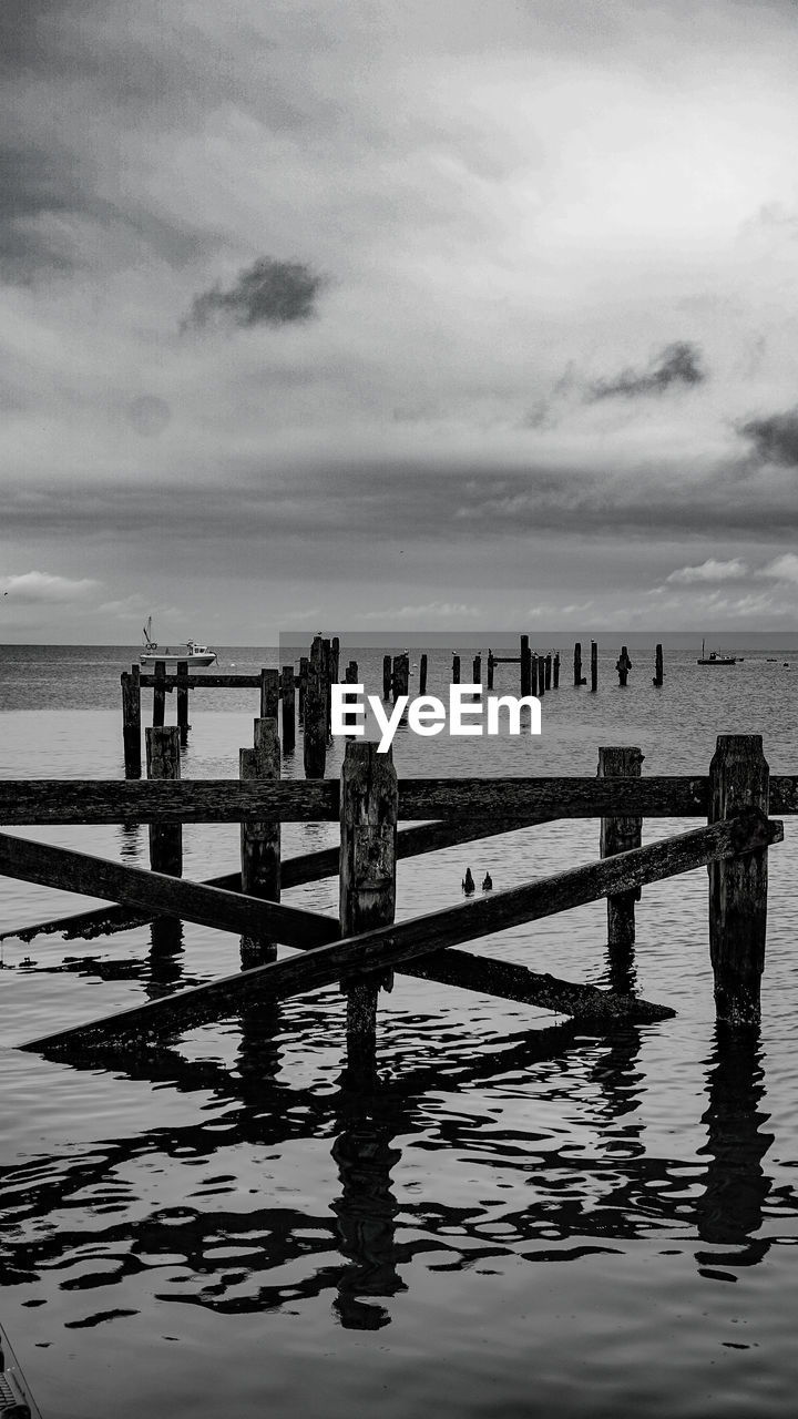 REFLECTION OF WOODEN POSTS IN SEA AGAINST SKY