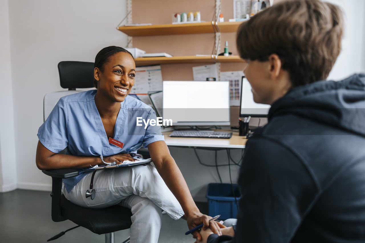 Happy medical professional consoling teenage patient while sitting in examination room at clinic