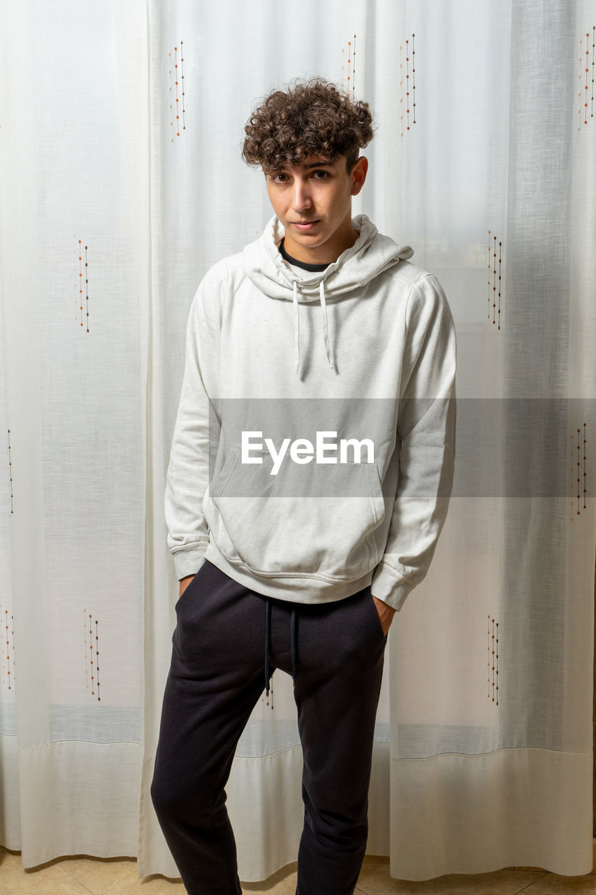 Portrait of young man standing against curtain