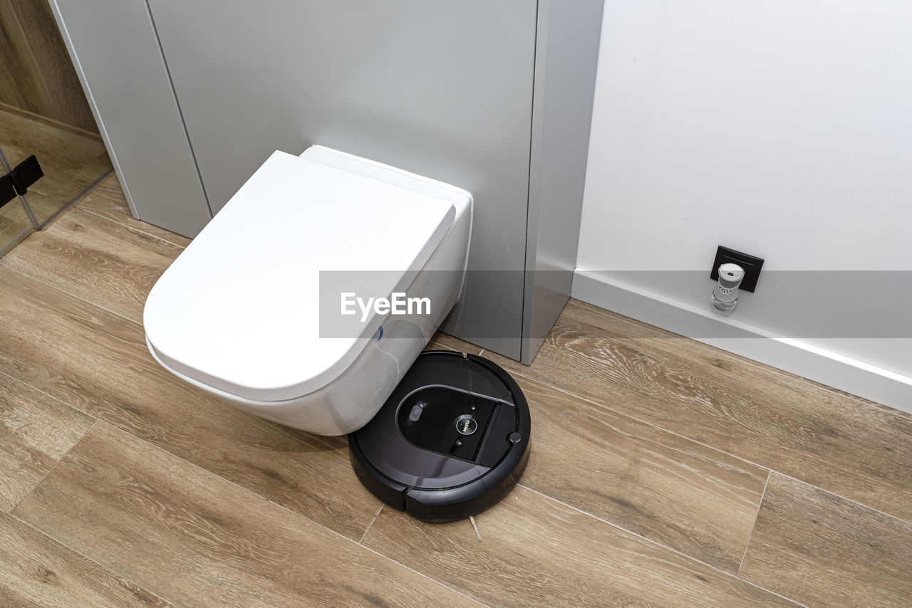 A modern robotic vacuum cleaner cleans the ceramic tiles in the bathroom next to the toilet. 
