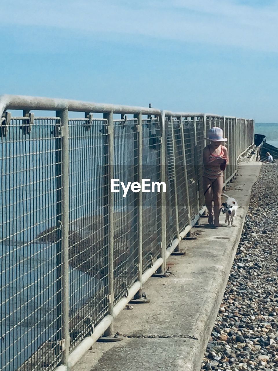 Full length of girl with dog walking on footpath at beach