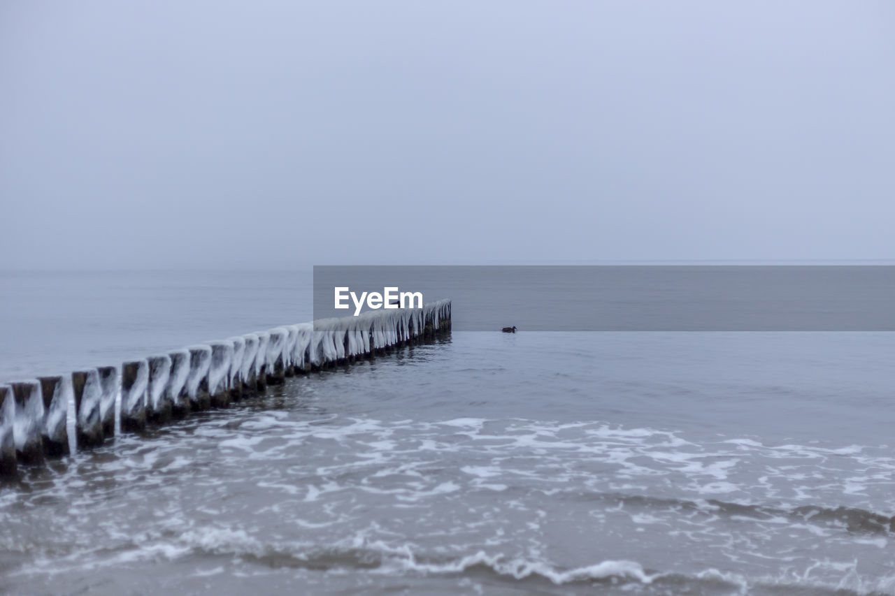 WOODEN POSTS ON PIER OVER SEA AGAINST CLEAR SKY