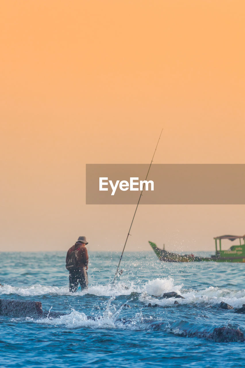 Man fishing in sea against sky