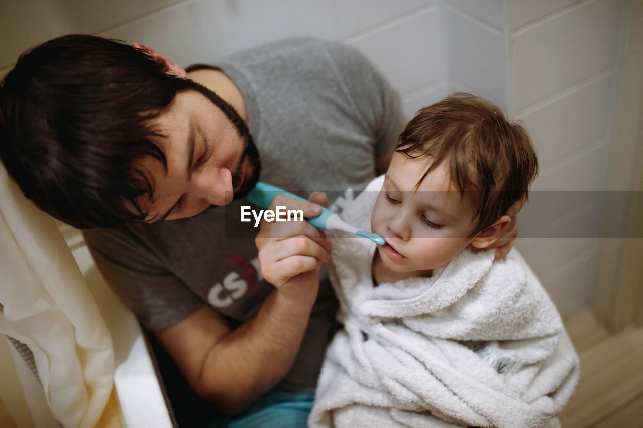 High angle view of father brushing teeth of son