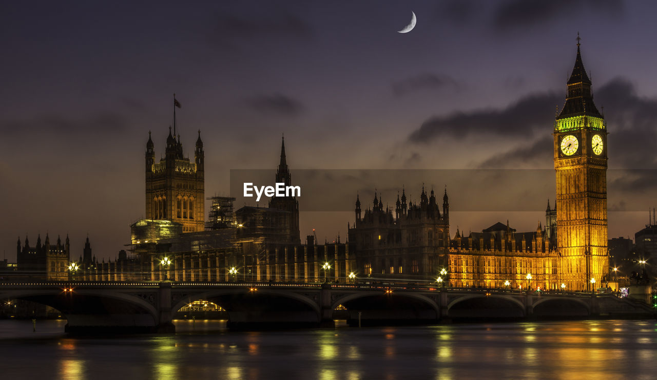 Scenic view of thames river by illuminated houses of parliament and westminster bridge against sky