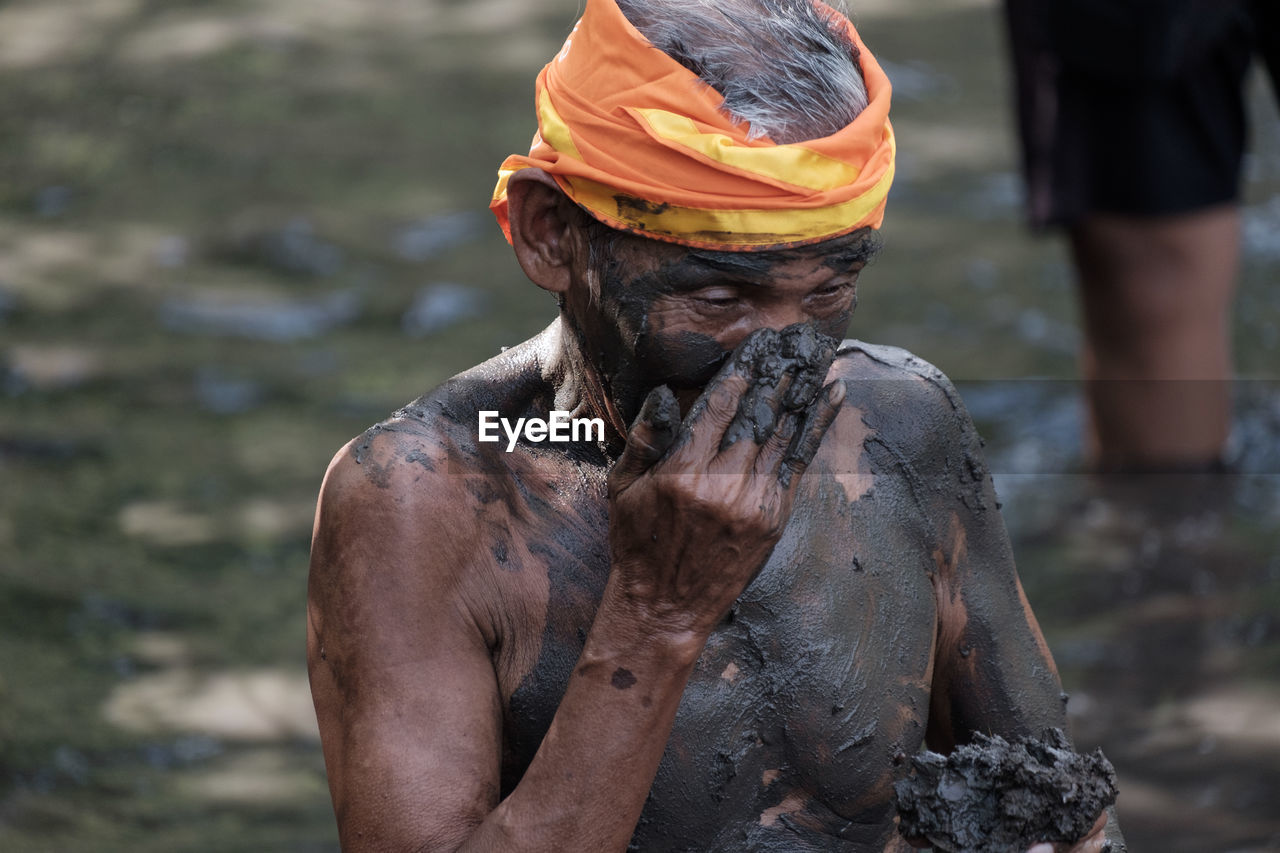 Close-up of shirtless man applying mud on body