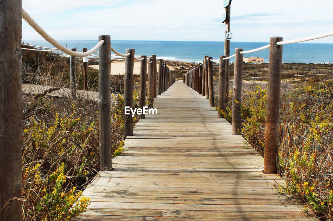 Wooden boardwalk amidst plants leading towards beach on sunny day
