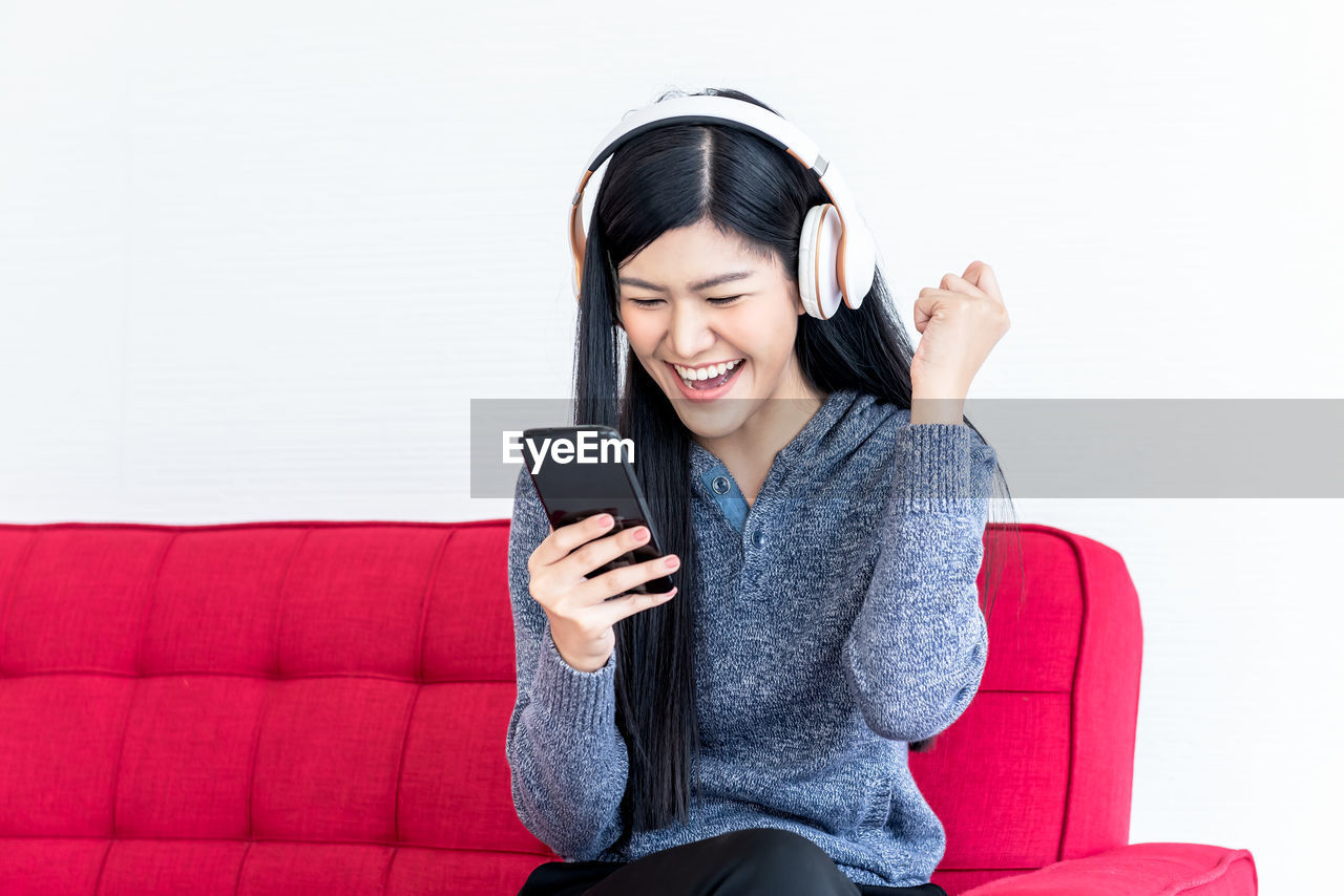 YOUNG WOMAN USING PHONE WHILE SITTING ON LAPTOP