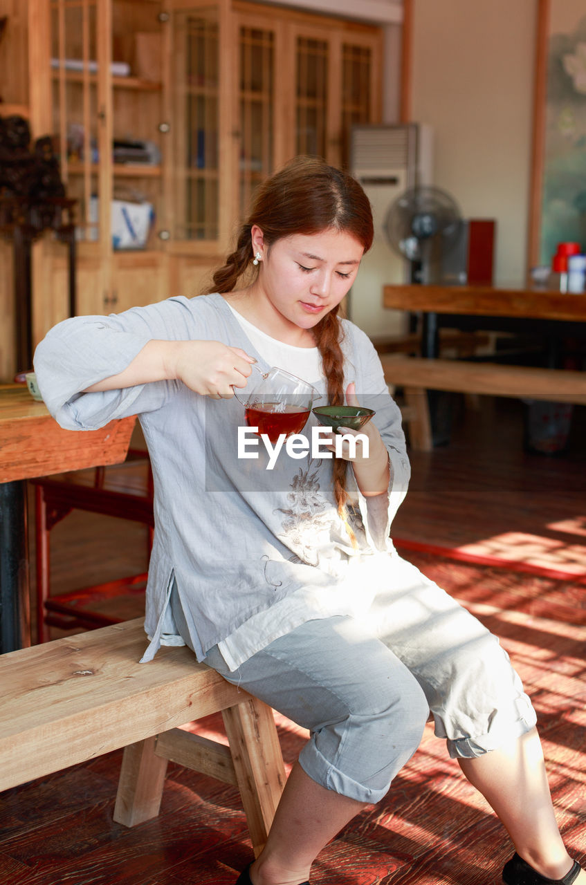 Girl making drink while sitting on wooden table at home