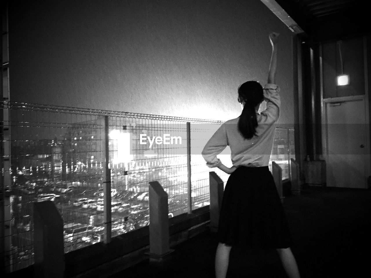 Rear view of woman with arm raised standing at balcony