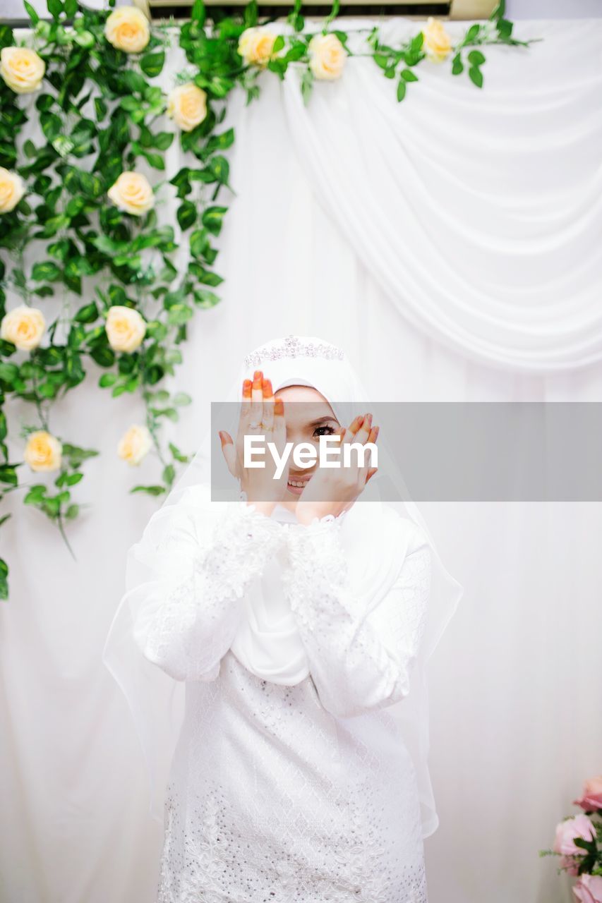 Portrait of bride gesturing while standing against curtain in wedding ceremony