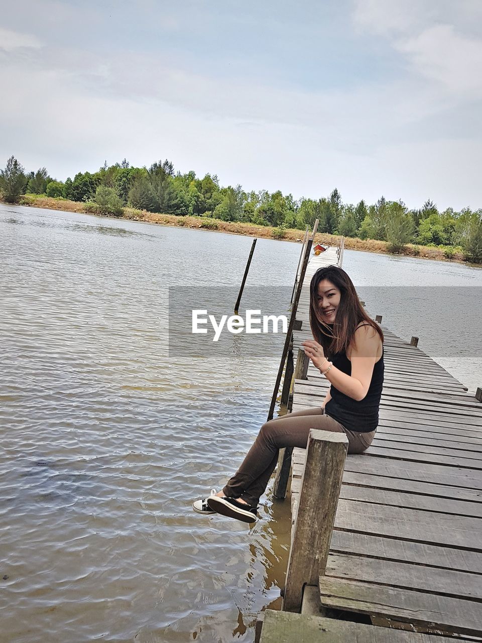 PORTRAIT OF WOMAN SITTING ON LAKE AGAINST SKY