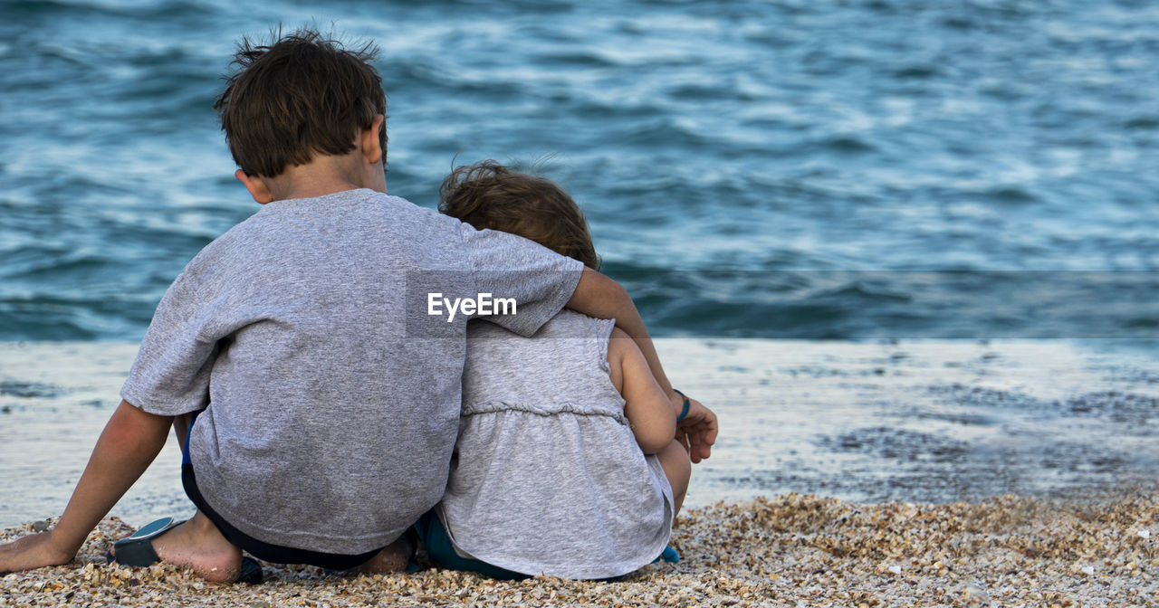 Rear view of siblings sitting at beach