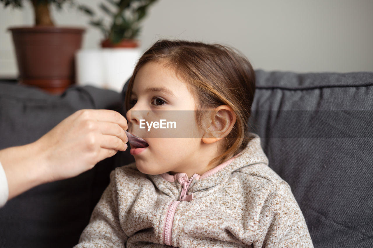 Cropped hand of mother feeding medicine to daughter