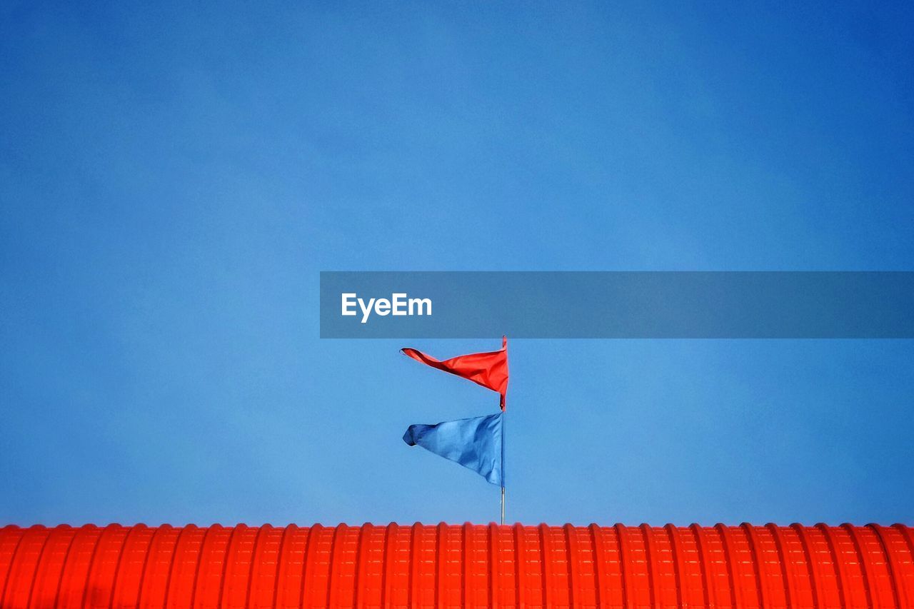 Low angle view of flags on red roof against blue sky