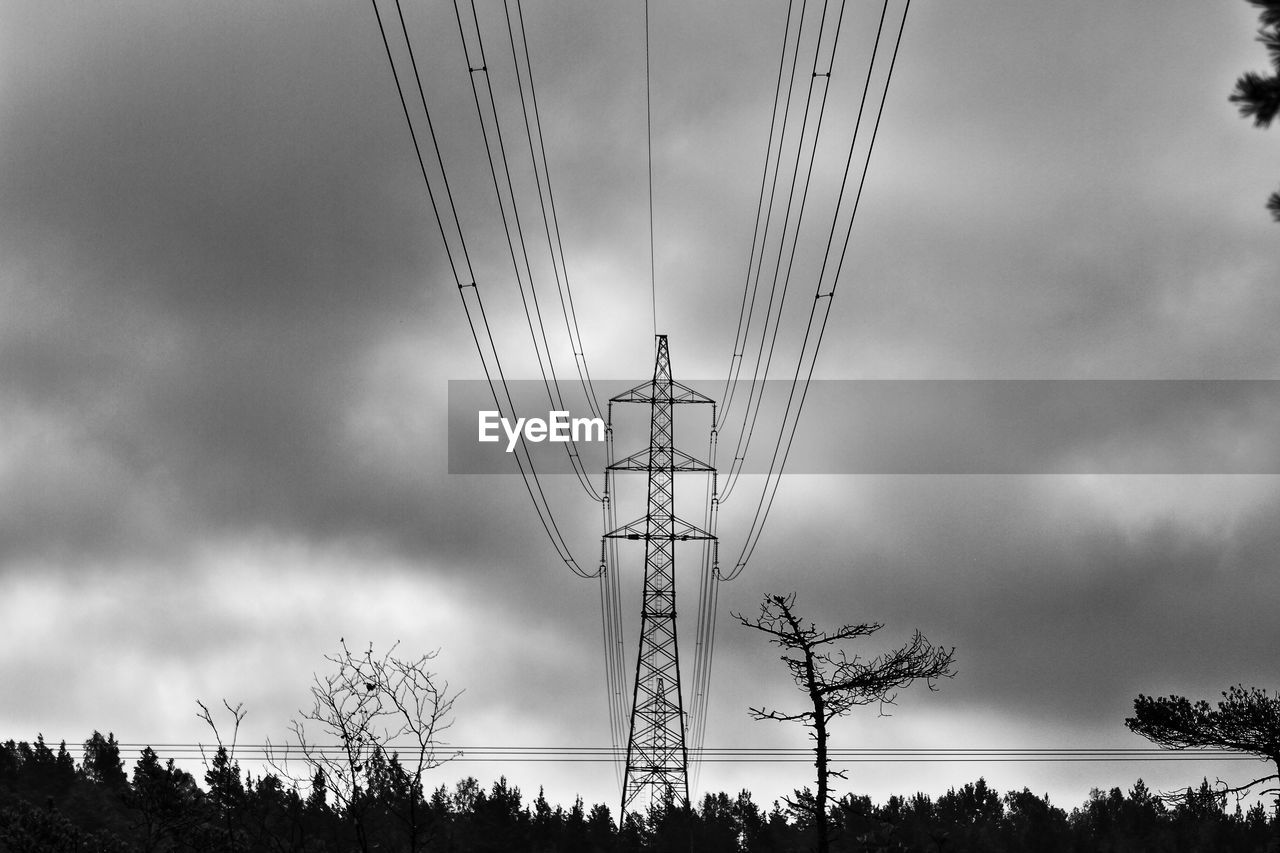 Low angle view of electricity pylon and trees and against cloudy sky