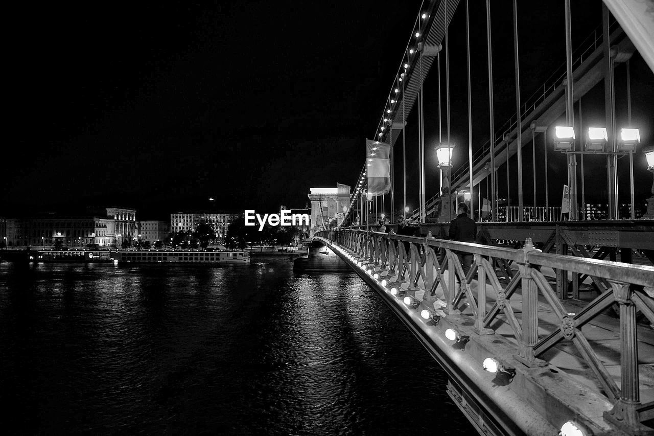 Illuminated bridge over river against sky at night