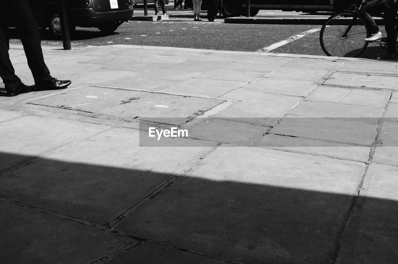 Low section of man standing on footpath during sunny day