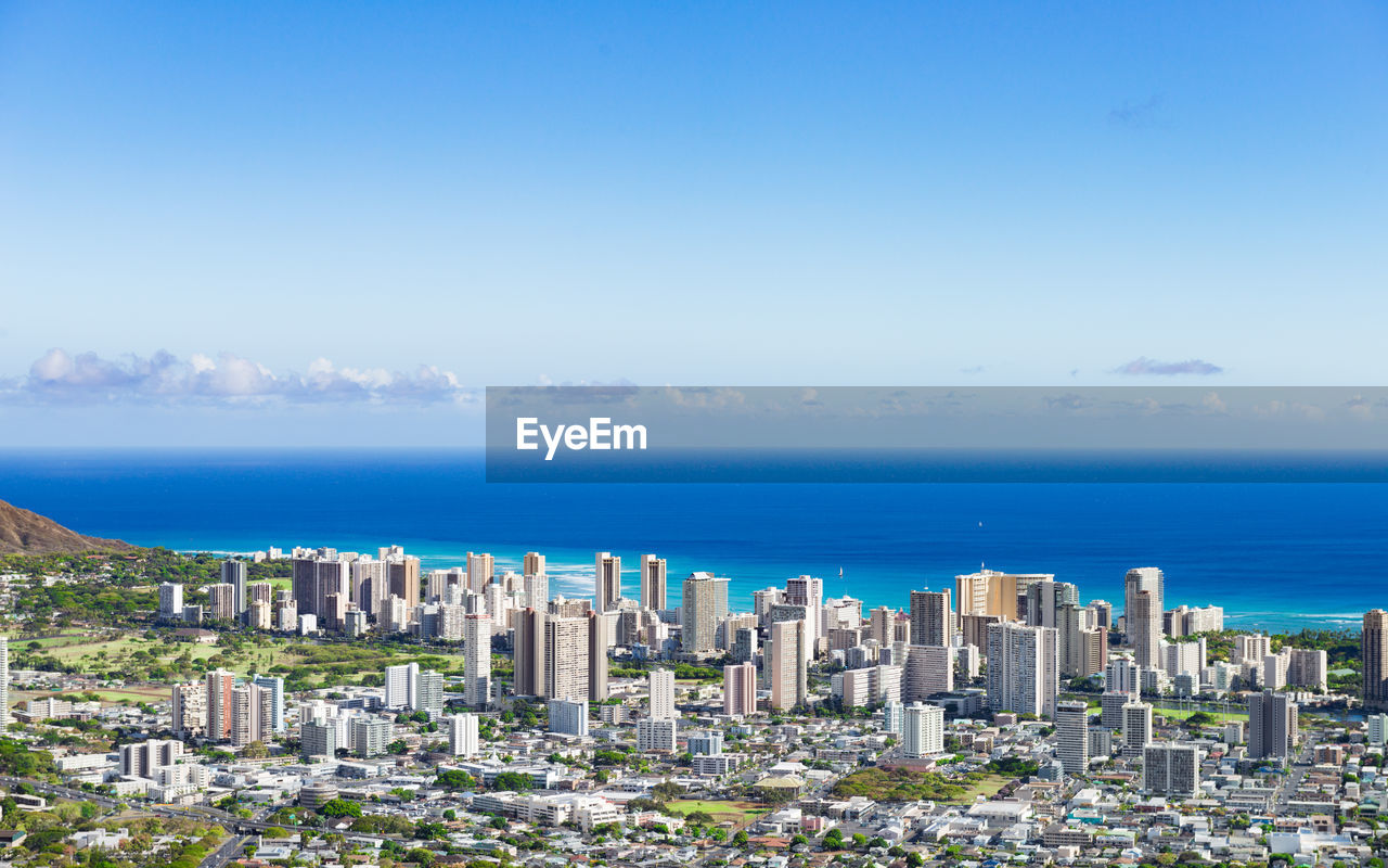 Cityscape by sea against blue sky