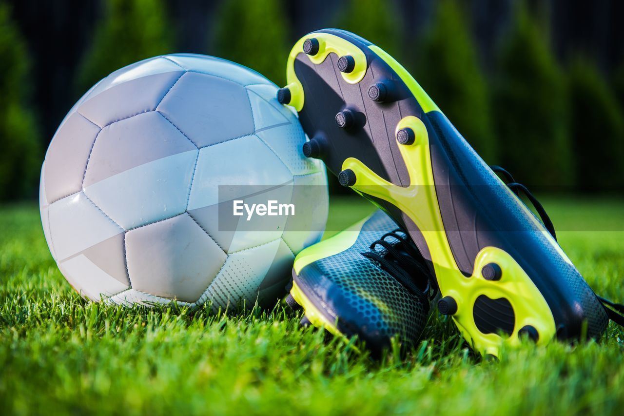 Close-up of soccer ball and sports shoes on field