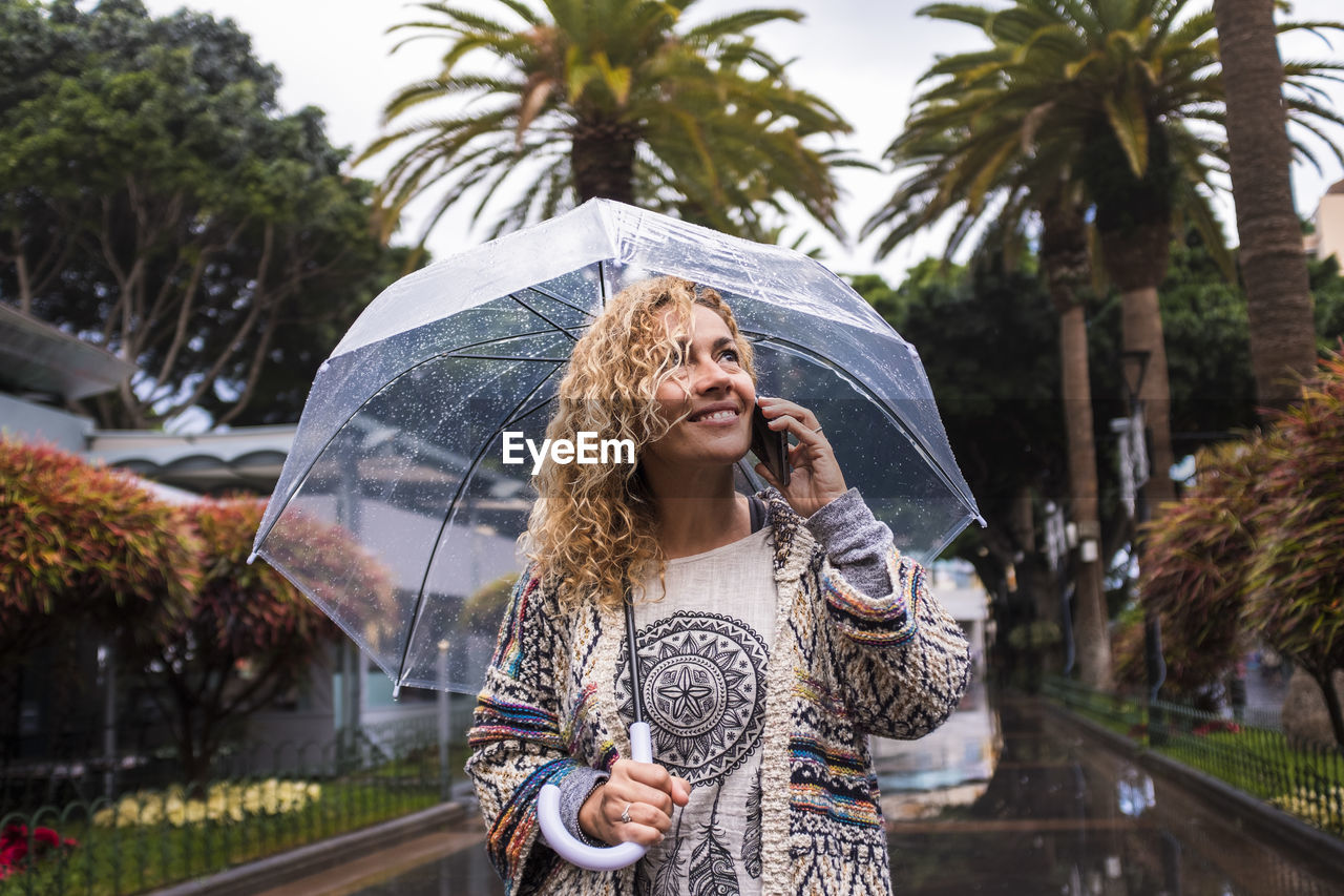 Woman with umbrella talking over phone while standing during rainy season