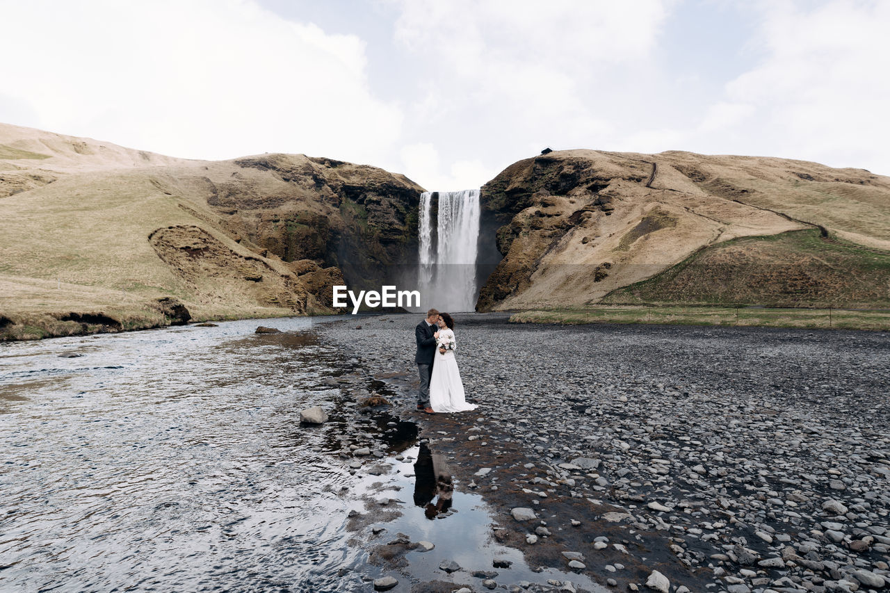 WOMAN STANDING ON ROCKS AGAINST SKY