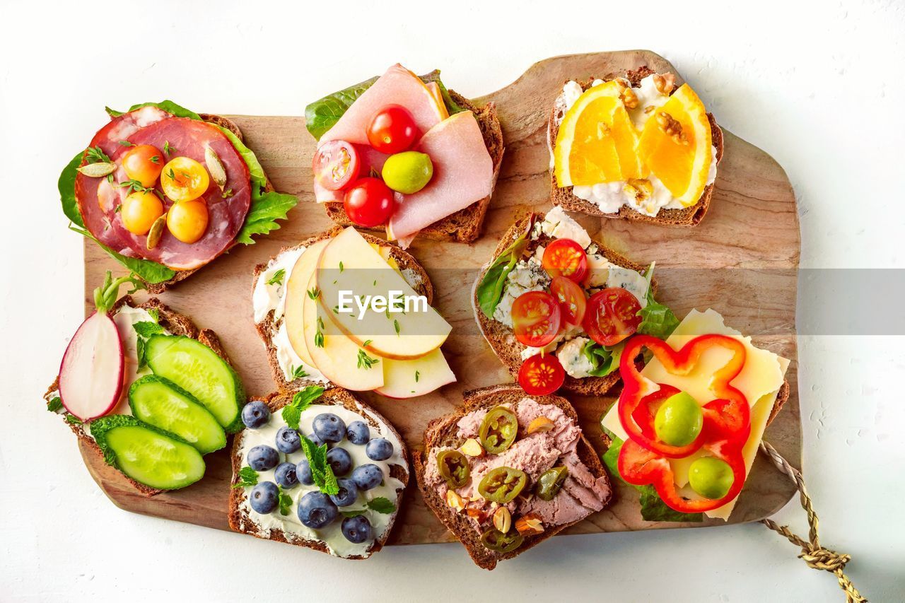 Assorted gourmet sandwiches on wooden board, top view