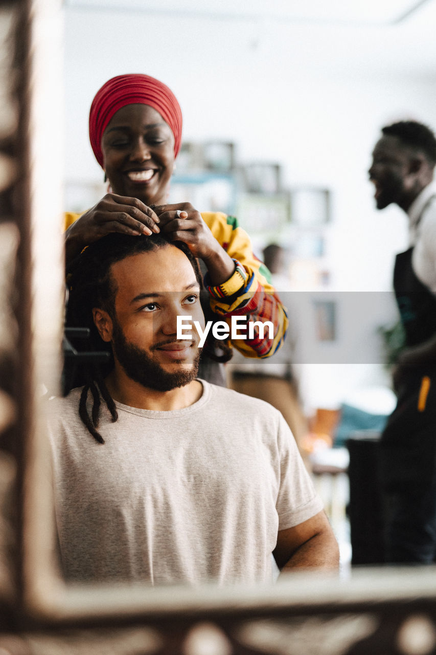 Happy female hairdresser making locs of male customer at barber shop