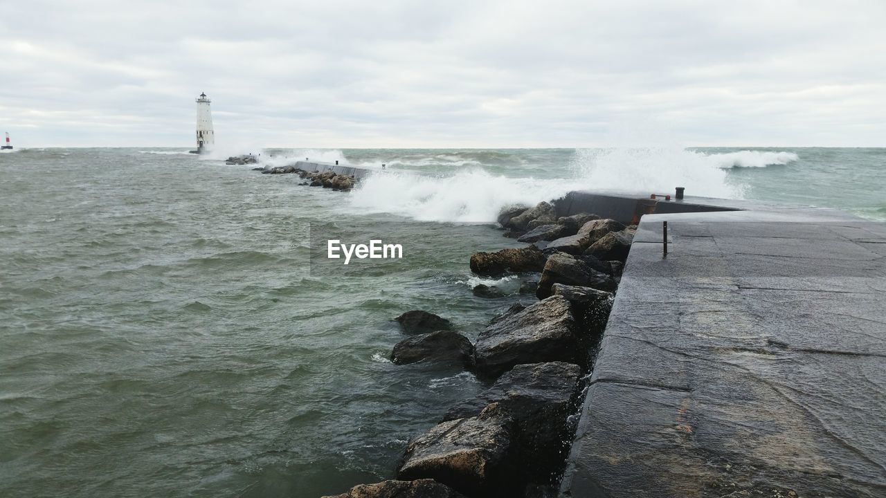 Waves splashing on groynes in sea against sky