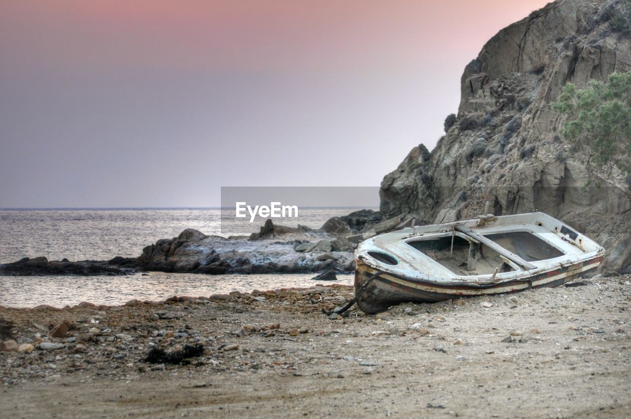 Abandoned boat on shore by rock formation against sky