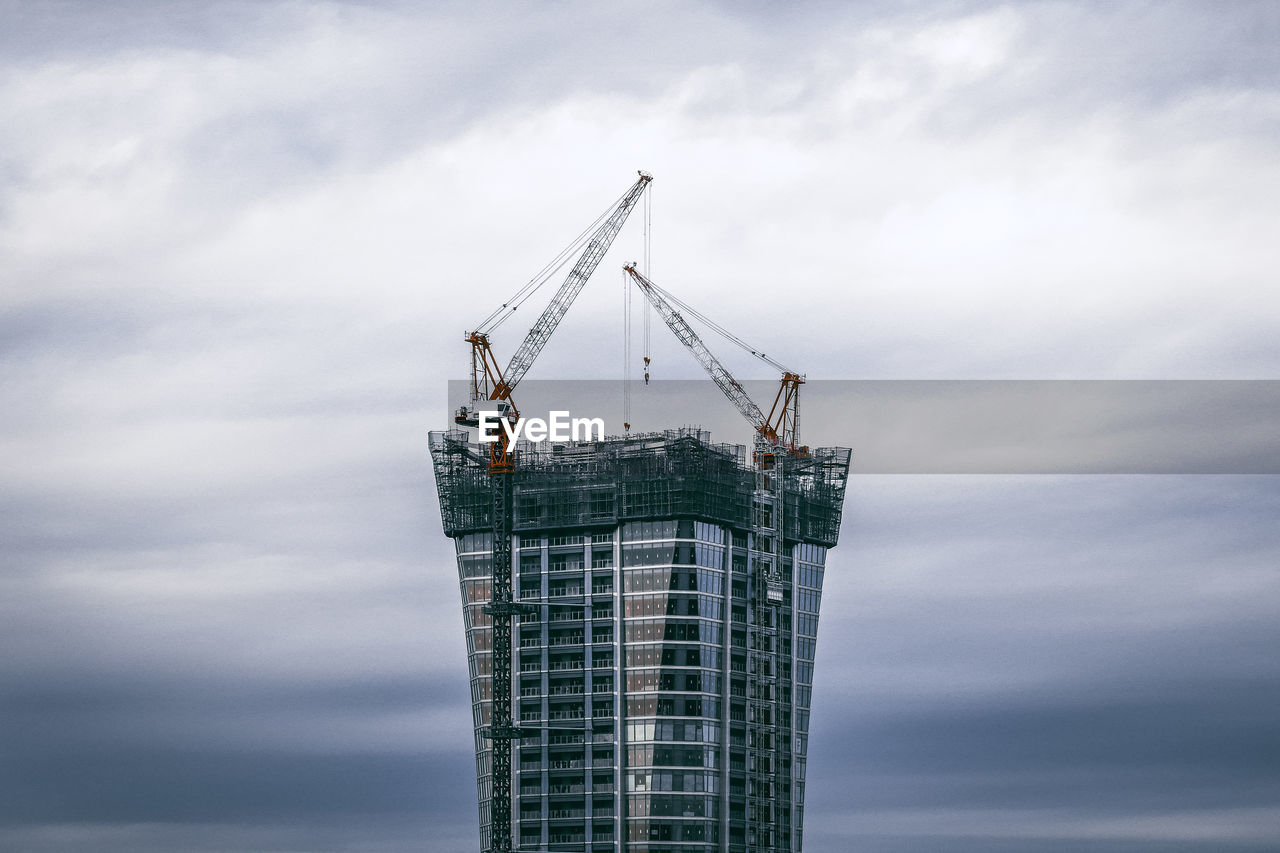 Low angle view of crane at construction site against sky