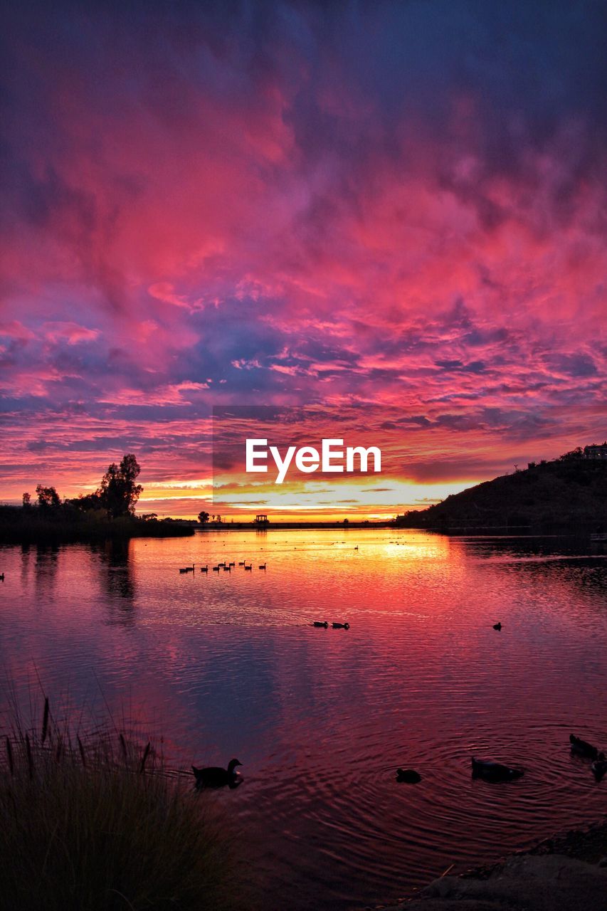 Scenic view of lake against dramatic sky during sunset