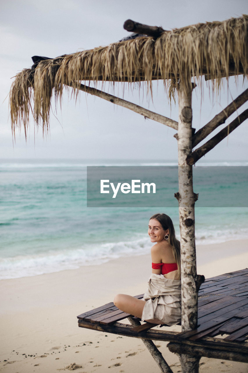 Woman sitting on beach by sea against sky