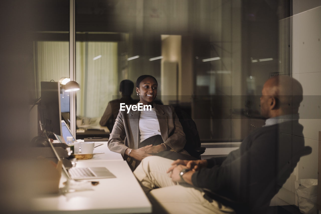 Smiling businesswoman planning strategy with male colleague seen through glass of work place