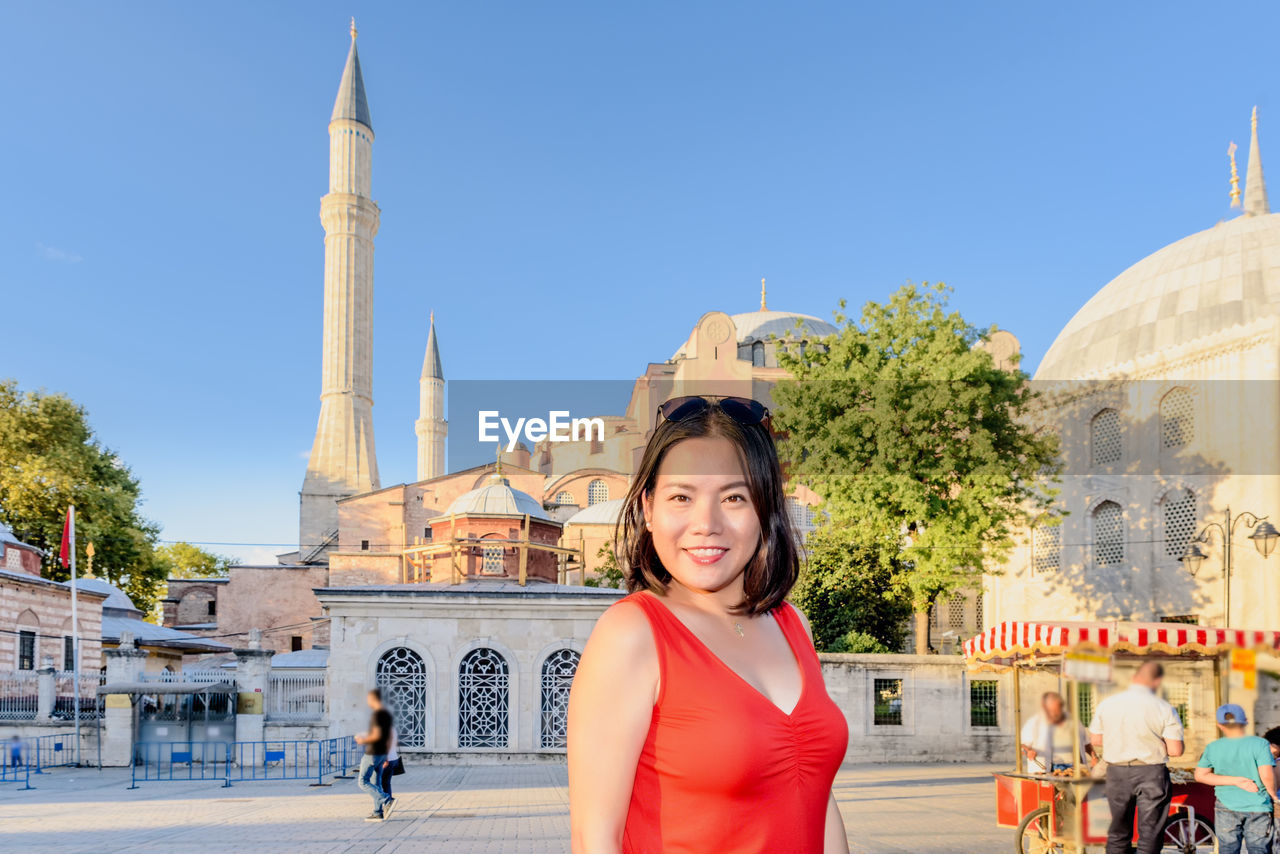 Portrait of smiling woman against mosque in city