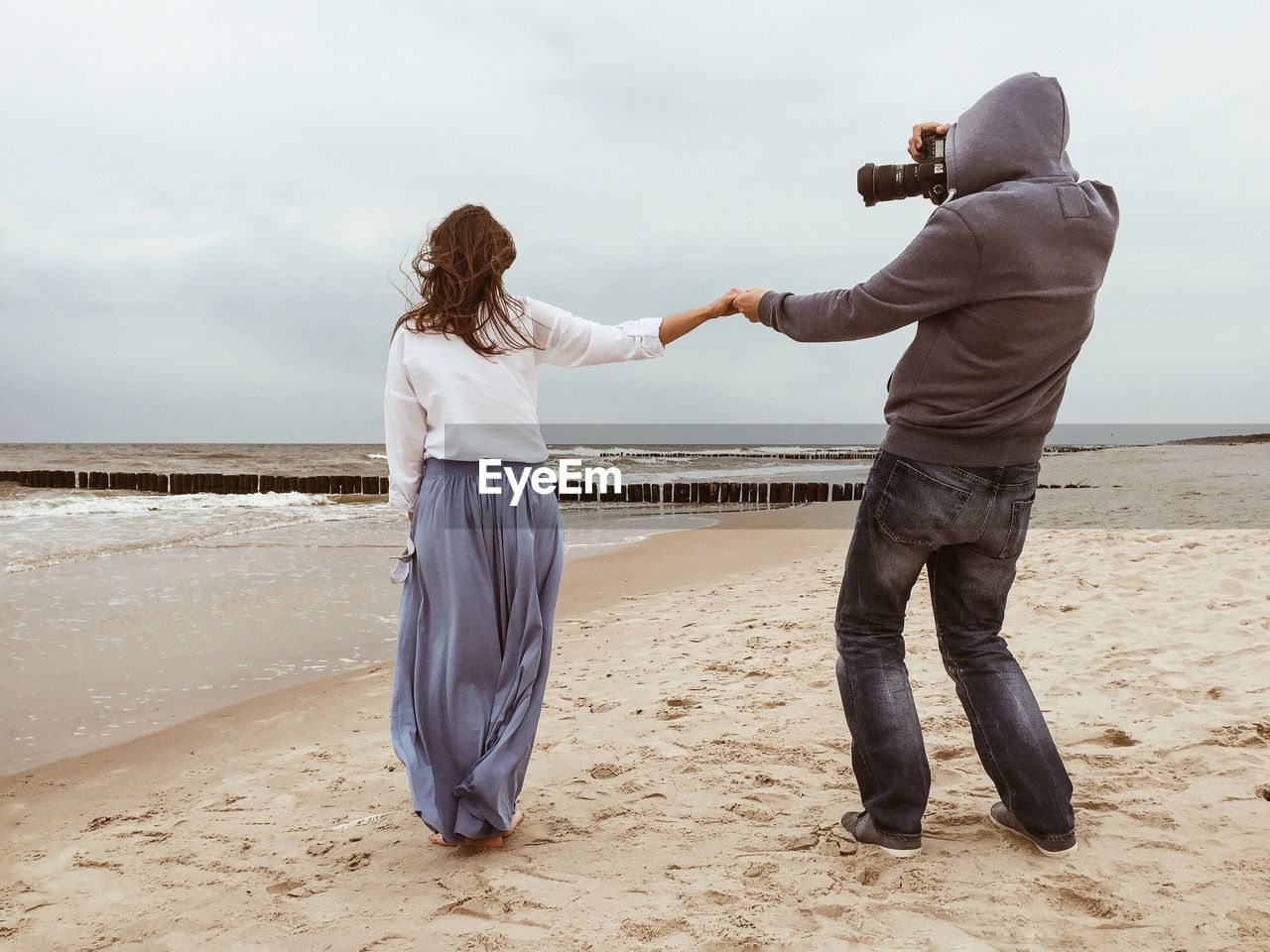 Man photographing woman at beach against sky