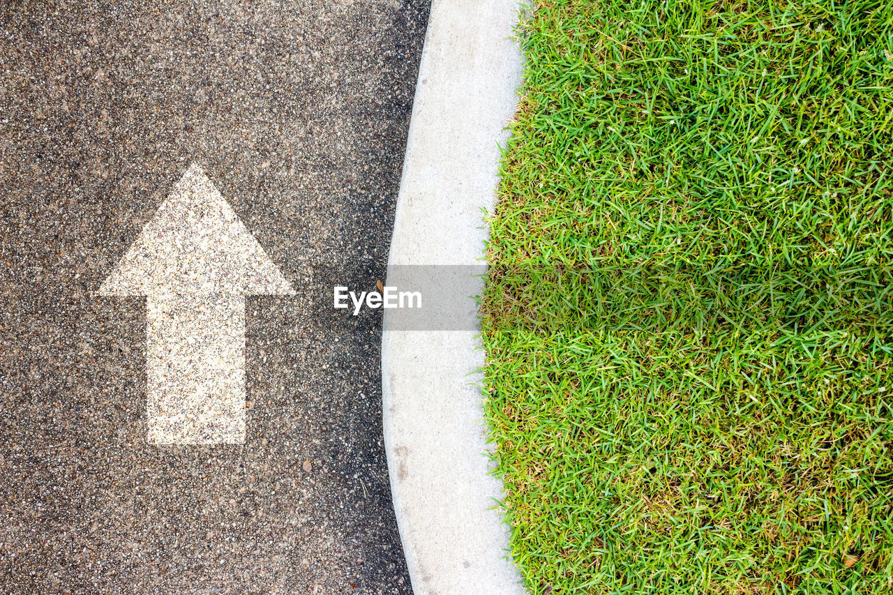 HIGH ANGLE VIEW OF ARROW SYMBOL ON GRASS ROAD